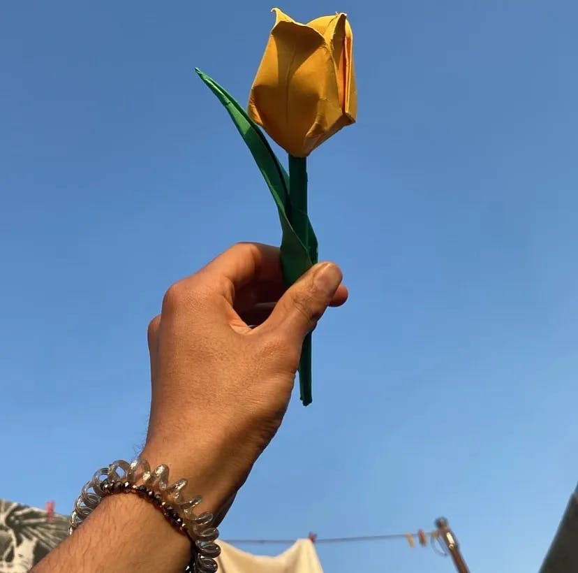 Fotografía de una flor de origami amarilla con el cielo azul de fondo.
