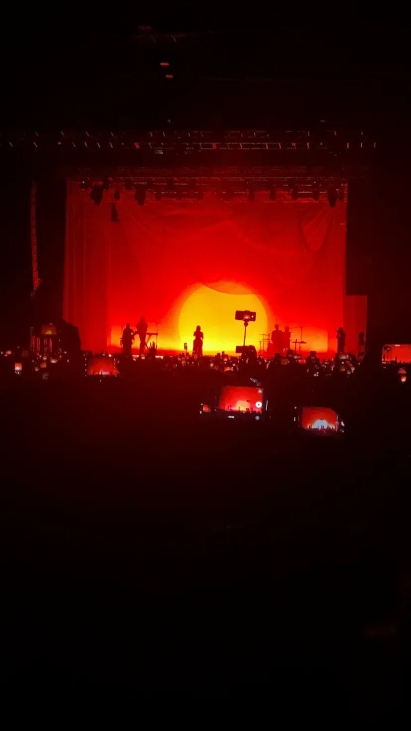Foto de un concierto de la artista Aurora donde se ve su silueta con un fondo rojo similar a un atardecer.